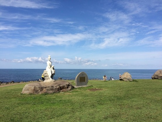 緑の草地に建つ白い乙女像　向こうには青い海　青い空　白い雲