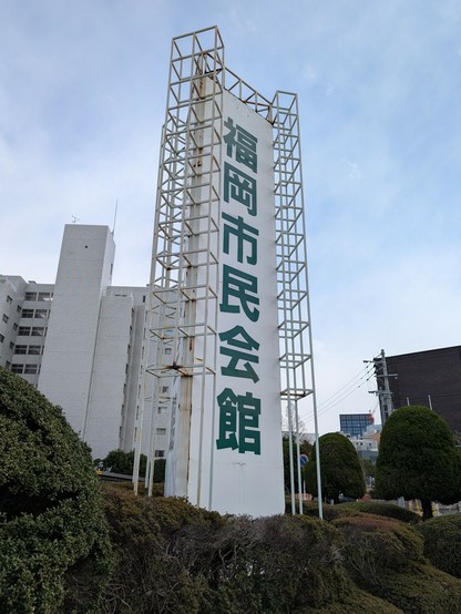 三角柱。白地に緑色の文字。「福岡市民会館」