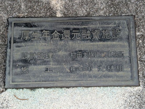 裏側に埋め込まれた説明板。「厚生年金還元融資施設／設計監理　村田大旗建築事務所／施工　株式会社大林組」